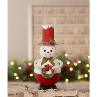 Decorative snowman figurine with a red top hat and wreath, standing on a wooden surface with a festive background.