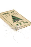 A square beige paper label or tag with green text reading 'XMAS TREE DECOR' and a green Christmas tree illustration, placed on a white background with scattered silver tinsel around it.