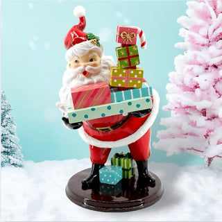 A festive Santa Claus figurine carrying multiple colorful gift boxes, set against a snowy winter backdrop with a light blue background and pink-tinted trees.